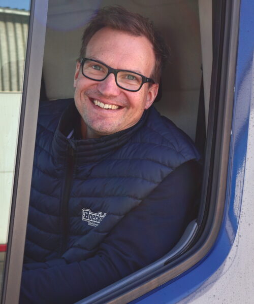 Marco Büren sitzt hinter dem Steuer eines Kleintransporters und blickt, freundlich lächelnd, aus dem Seitenfenster des Kleintransporters heraus.