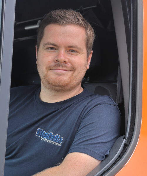 Jan Kauert sitzt hinter dem Steuer eines Kleintransporters und blickt, freundlich lächelnd, aus dem Seitenfenster des Kleintransporters heraus.